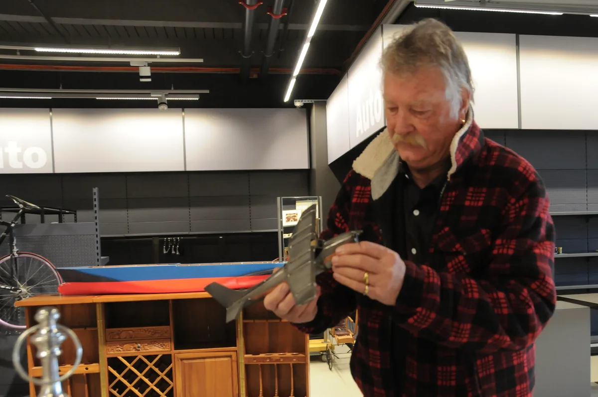 Dieser Herr kommt fast täglich vorbei, um durch das ständig wechselnde Sortiment zu stöbern. Man sieht einen älteren Mann, der ein Deko-Flugzeug in den Händen hält.